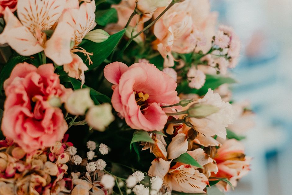 A floral arrangement featuring a variety of fresh summer flowers, including pink and peach roses, bloom-shaped lisianthus with soft pink petals, and small white blossoms, assembled into a lush bouquet